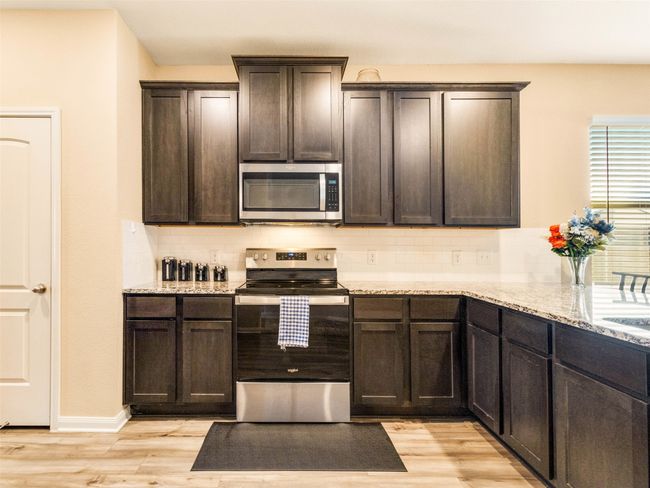 Kitchen with light stone counters, dark brown cabinets, light wood-type flooring, stainless steel appliances, and decorative backsplash | Image 11