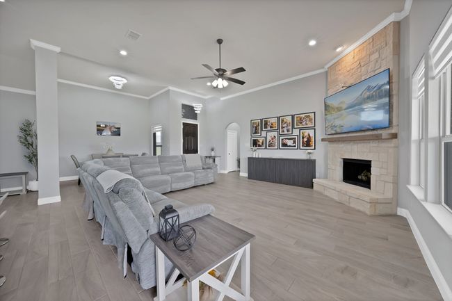 Living room with arched walkways, ornamental molding, ceiling fan, a fireplace, and baseboards | Image 11