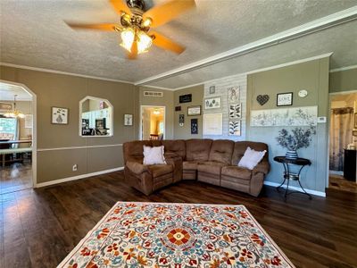 Living room with a textured ceiling, dark wood-type flooring, ceiling fan with notable chandelier, and crown molding | Image 3