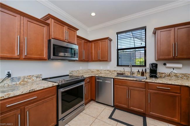 Kitchen with crown molding, appliances with stainless steel finishes, a sink, light tile patterned floors, and light stone counters | Image 8