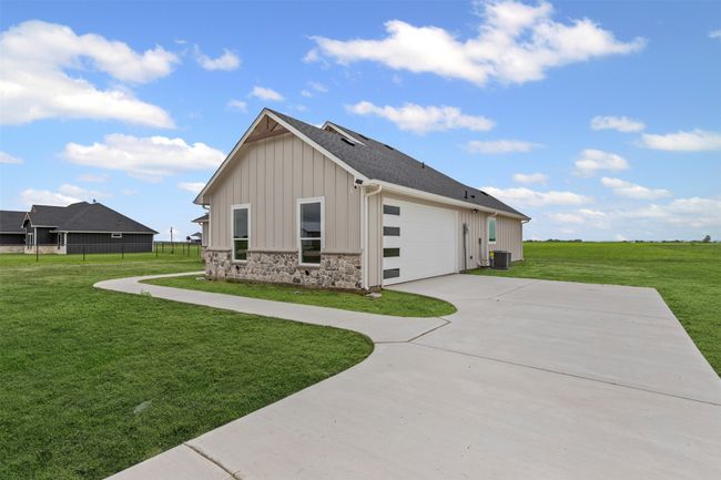 View of property exterior with board and batten siding, driveway, central air condition unit, a yard, and stone siding | Image 5