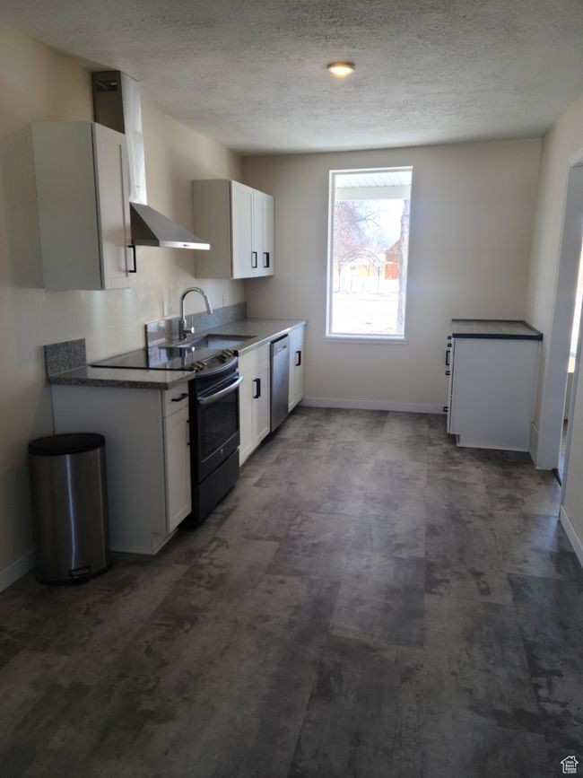 Kitchen featuring electric range oven, stainless steel dishwasher, baseboards, a sink, and a textured ceiling | Image 10