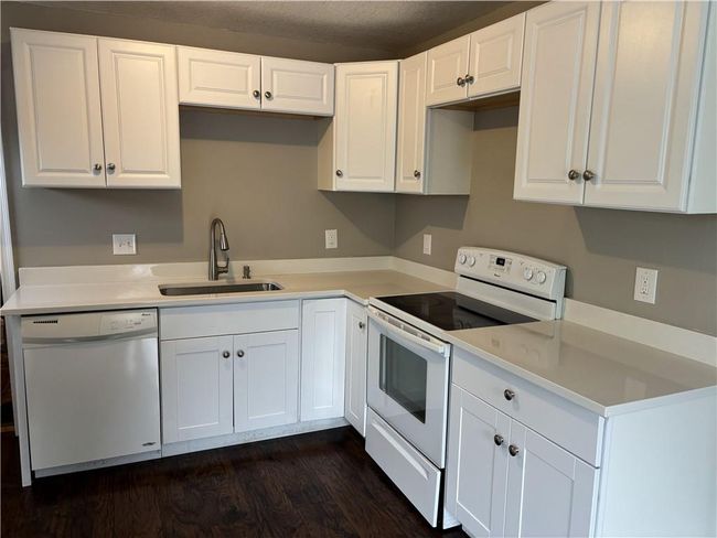 Kitchen with dark wood-type flooring, white appliances, white cabinets, and a sink | Image 9