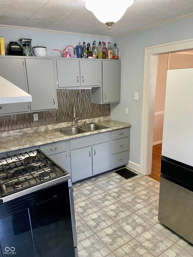kitchen featuring freestanding refrigerator, light countertops, a sink, black range with gas stovetop, and crown molding | Image 10