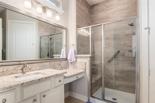 This bathroom features a modern design with a spacious glass-enclosed shower, elegant tile work, and a granite countertop with ample storage. The large mirror and stylish lighting enhance the bright, clean look. | Image 8