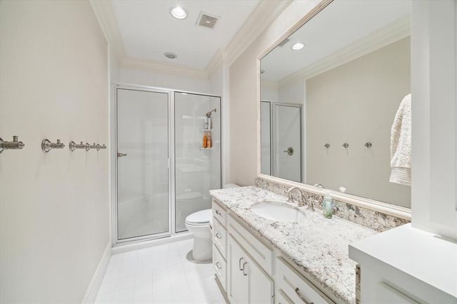 This bathroom features a sleek design with a large walk-in shower, elegant granite countertop, and ample storage space under the sink. The neutral color palette and recessed lighting create a bright and inviting atmosphere. | Image 27