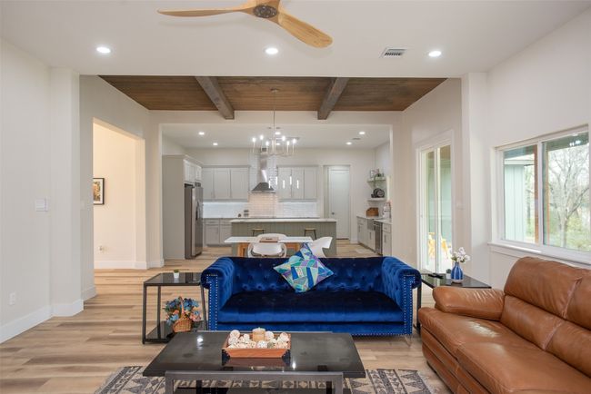 Living room featuring beamed ceiling, light wood-type flooring, ceiling fan with notable chandelier, and wooden ceiling | Image 18