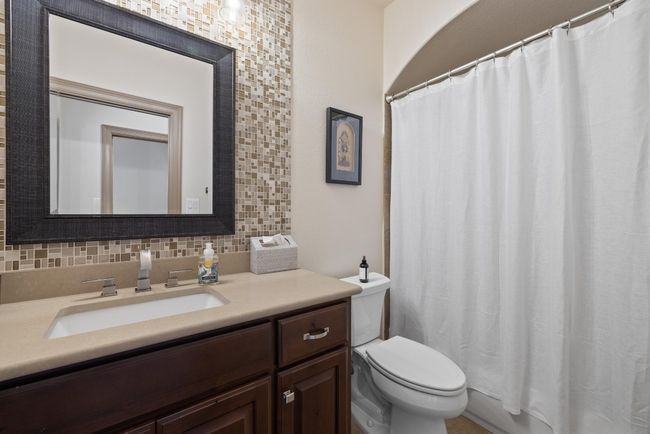 Bathroom with toilet, vanity, decorative backsplash, and curtained shower | Image 24