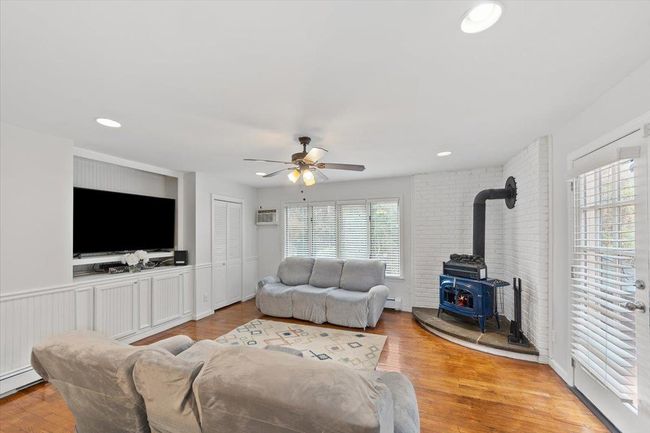 Living room with light wood-style flooring, ceiling fan, recessed lighting, a wood stove, and an AC wall unit | Image 34