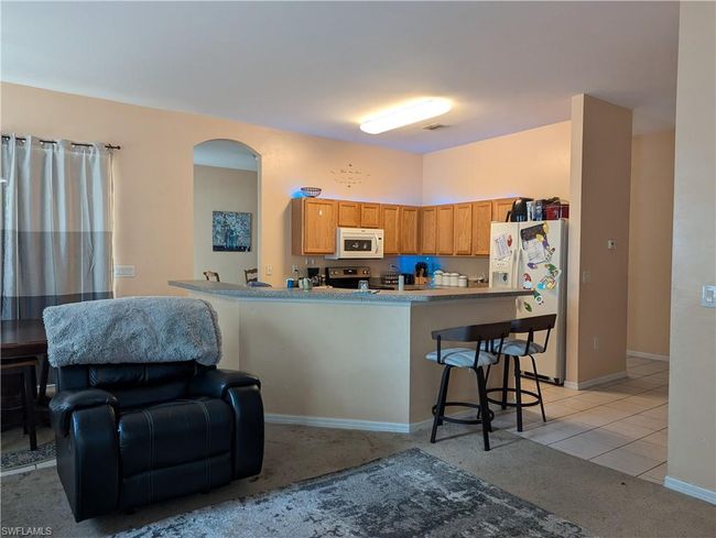 Kitchen with white appliances, arched walkways, light colored carpet, a kitchen bar, and a peninsula | Image 24