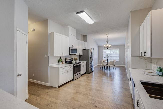 Kitchen with stainless steel appliances, a chandelier, light wood-style floors, white cabinets, and a textured ceiling | Image 15