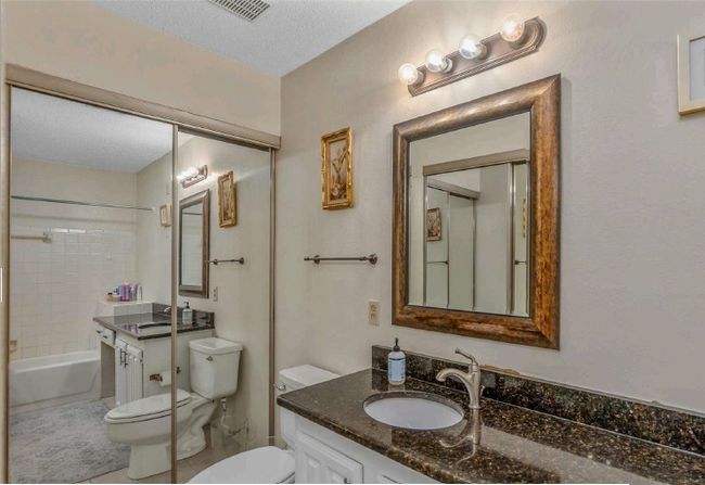 Full bath featuring a textured ceiling, shower combination, toilet, visible vents, and vanity | Image 19