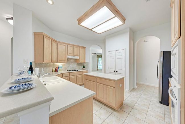 Kitchen featuring light brown cabinets, white appliances, backsplash, arched walkways, and a sink | Image 16