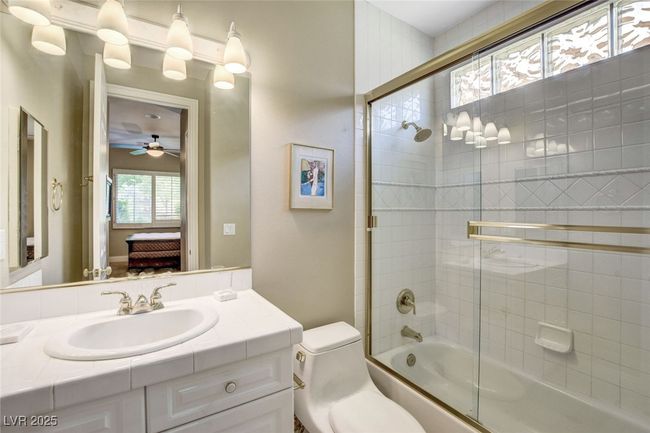 Bathroom with bath / shower combo with glass door, connected bathroom, toilet, vanity, and a ceiling fan | Image 37