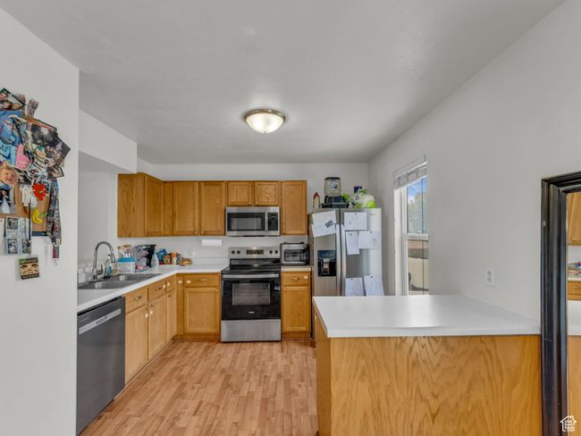 Kitchen featuring stainless steel appliances, a sink, light wood-type flooring, light countertops, and a peninsula | Image 10