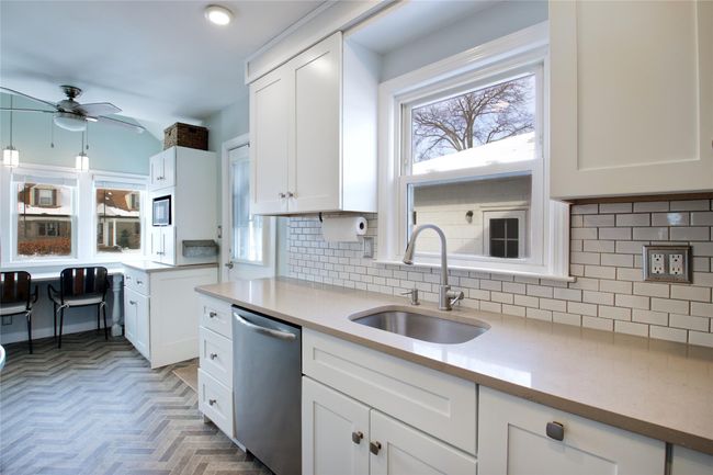 Kitchen with stainless steel dishwasher, a sink, ceiling fan, white cabinets, and decorative backsplash | Image 12