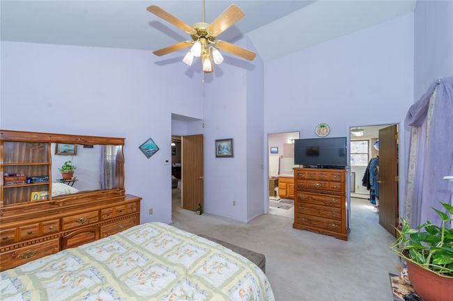 Bedroom with light colored carpet, a baseboard radiator, ceiling fan, ensuite bathroom, and high vaulted ceiling | Image 26