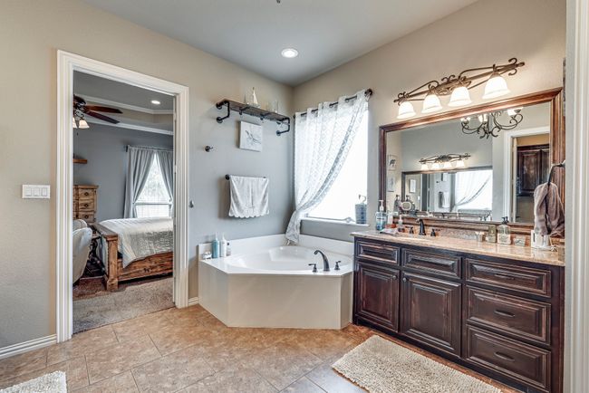 Primary bathroom with double vanity, ornamental molding, ceiling fan with notable chandelier, and a wealth of natural light | Image 6
