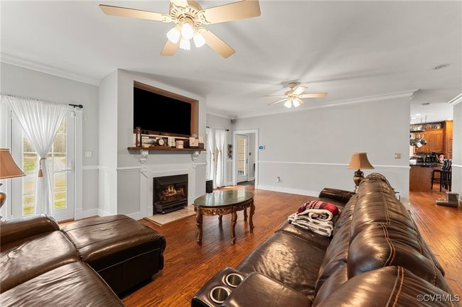 Living room with a ceiling fan, wood finished floors, crown molding, and a fireplace with flush hearth | Image 6