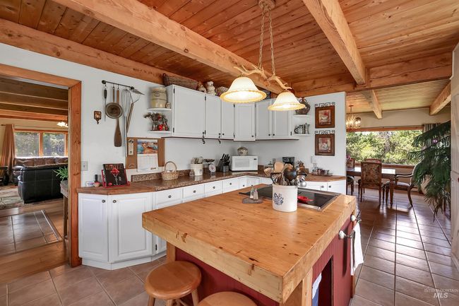 Kitchen with open shelves, butcher block countertops, light tile patterned flooring, a wooden ceiling with exposed beams, and white cabinetry | Image 18