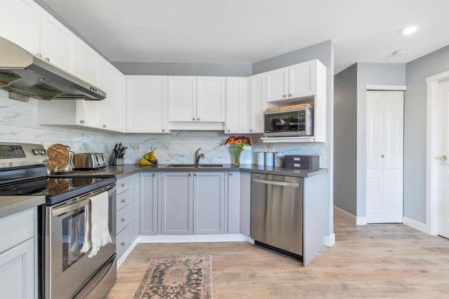 Kitchen with light wood-type flooring, under cabinet range hood, a sink, backsplash, and appliances with stainless steel finishes | Image 15