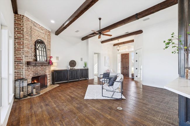 Living area featuring a ceiling fan, beam ceiling, wood finished floors, a fireplace, and baseboards | Image 8