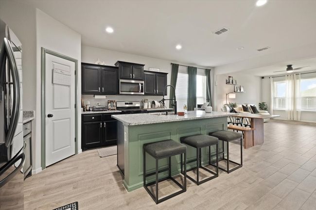 Kitchen featuring stainless steel appliances, a kitchen bar, dark cabinets, a kitchen island with sink, and light ceramic tile floors | Image 11