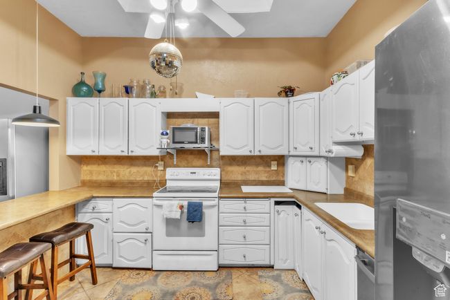 Kitchen featuring appliances with stainless steel finishes, ceiling fan, decorative backsplash, white cabinetry, and hanging light fixtures | Image 11
