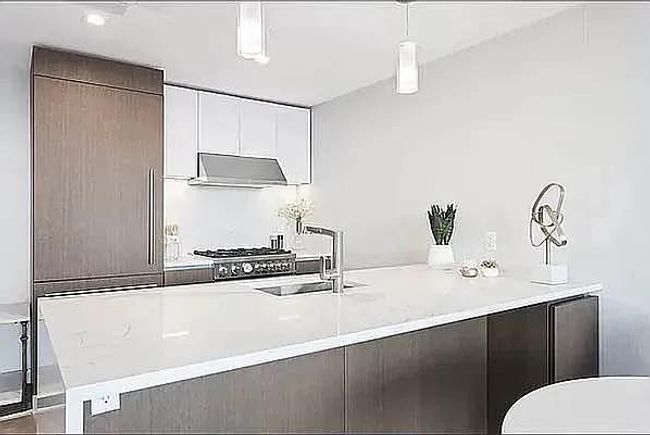 Kitchen featuring a sink, modern cabinets, under cabinet range hood, light countertops, and decorative light fixtures | Image 4