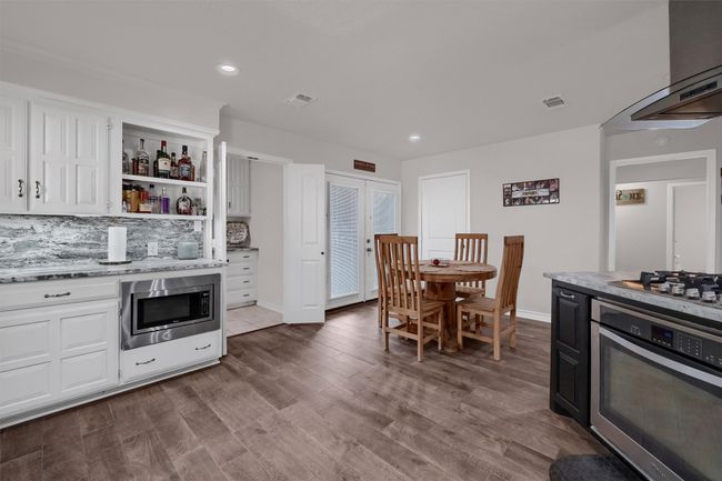 Kitchen featuring stainless steel appliances, light stone counters, tasteful backsplash, exhaust hood, and open shelves | Image 11