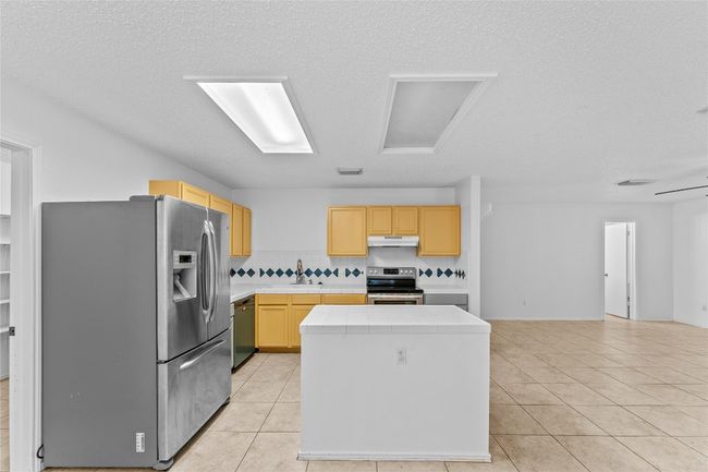 Kitchen with appliances with stainless steel finishes, under cabinet range hood, light brown cabinets, a center island, and light tile patterned floors | Image 14
