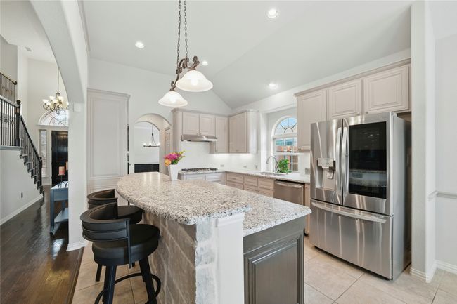 Kitchen with appliances with stainless steel finishes, a chandelier, a kitchen island, arched walkways, and light stone countertops | Image 11