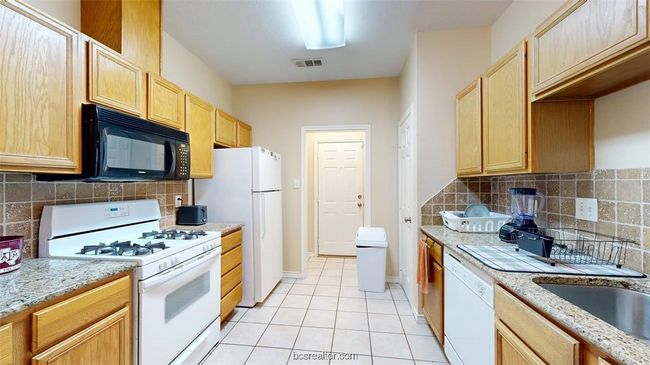 Kitchen with light brown cabinetry, tasteful backsplash, white appliances, and light tile patterned flooring | Image 7