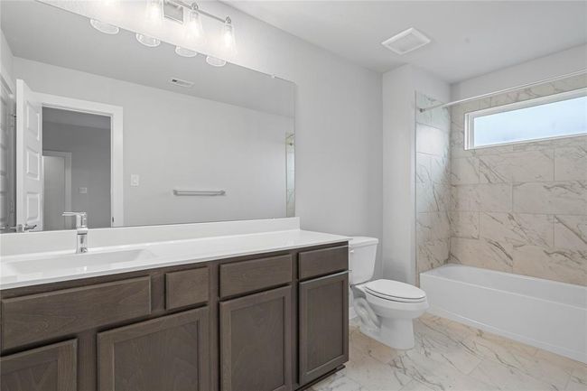 Secondary bath features tile flooring, bath/shower combo with tile surround, stained wood cabinets, beautiful light countertops, mirror, dark, sleek fixtures and modern finishes. | Image 21