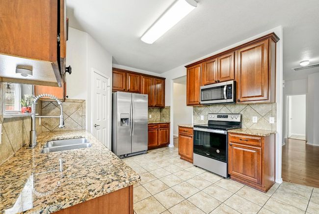 Kitchen featuring stainless steel appliances, decorative backsplash, light tile patterned flooring, and light stone counters | Image 7