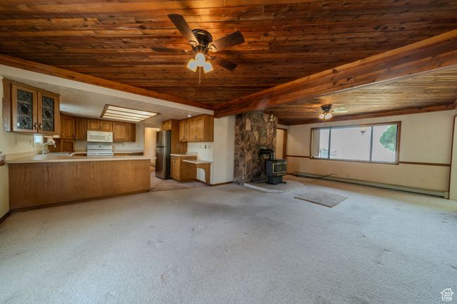 Unfurnished living room featuring a sink, light colored carpet, ceiling fan, wooden ceiling, and a wood stove | Image 7