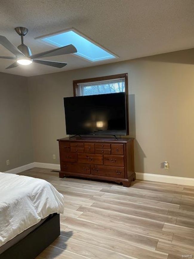 Bedroom with ceiling fan, a skylight, light hardwood / wood-style floors, and a textured ceiling | Image 8