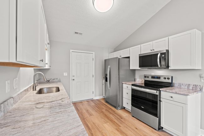 Kitchen featuring stainless steel appliances, lofted ceiling, white cabinets, light wood-style floors, and a textured ceiling | Image 13