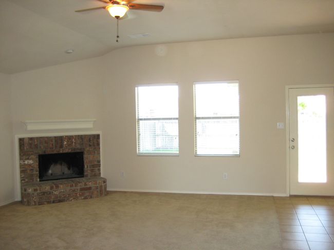 Unfurnished living room with healthy amount of natural light, a ceiling fan, a brick fireplace, lofted ceiling, and light tile patterned floors | Image 4
