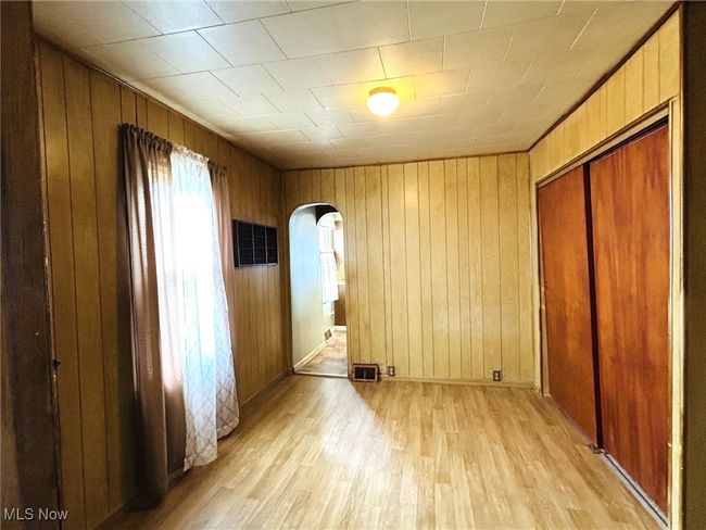 Unfurnished bedroom featuring arched walkways, light wood-style flooring, wooden walls, and a closet | Image 8