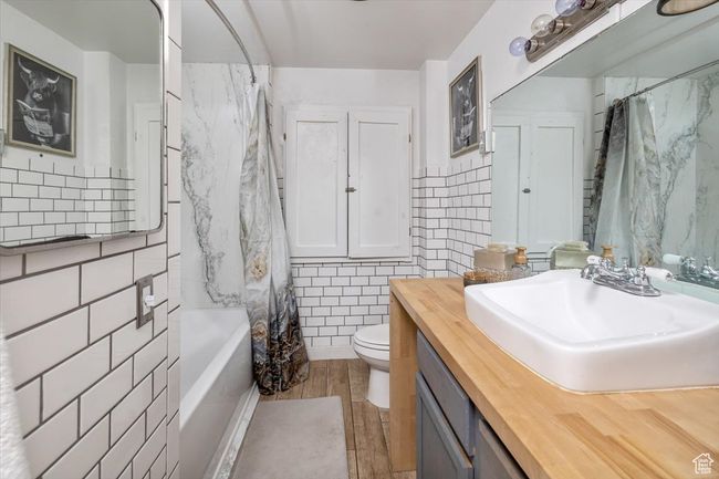 Full bathroom with toilet, hardwood / wood-style floors, shower / bath combo with shower curtain, tile walls, and vanity | Image 15