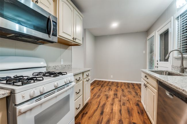 Kitchen with appliances, shelves, light wood-look flooring, and light stone counters looking towards eating area. | Image 12