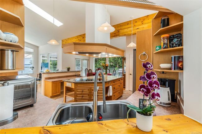 Kitchen featuring open shelves, a sink, wall chimney range hood, a kitchen island with sink, and a skylight | Image 10