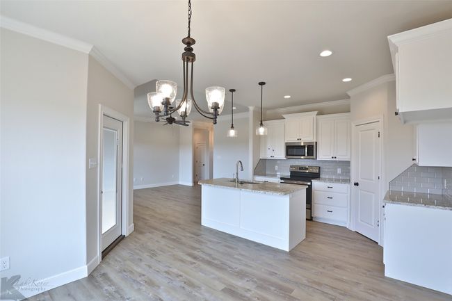 Kitchen featuring stainless steel appliances, ornamental molding, a chandelier, decorative backsplash, and white cabinetry | Image 10
