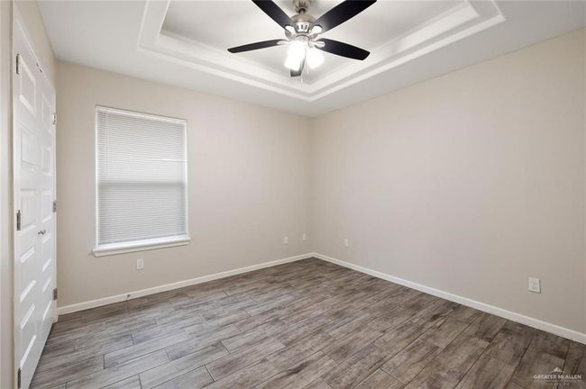 Unfurnished room with a tray ceiling, wood finished floors, and ceiling fan | Image 5