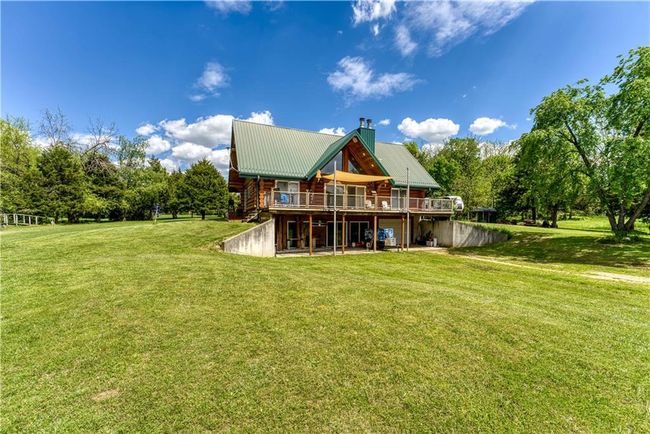 Rear view of house featuring metal roof, a chimney, a deck, and a lawn | Image 6
