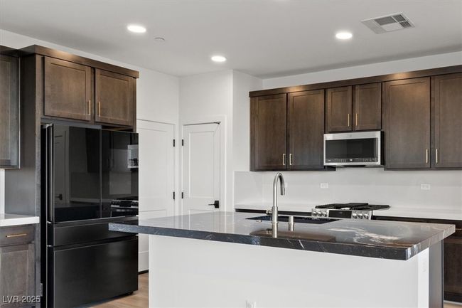 Kitchen with stainless steel microwave, a sink, visible vents, dark brown cabinets, and freestanding refrigerator | Image 26
