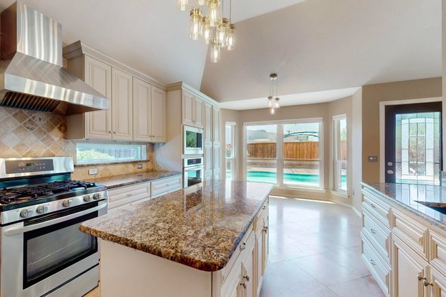 Kitchen with wall chimney exhaust hood, appliances with stainless steel finishes, a healthy amount of sunlight, dark stone counters, and backsplash | Image 13