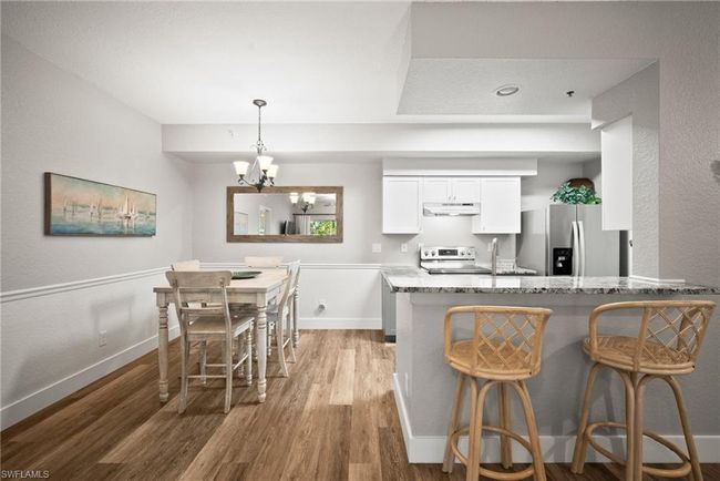 Kitchen featuring stainless steel appliances, under cabinet range hood, a chandelier, light stone countertops, and wood finished floors | Image 31