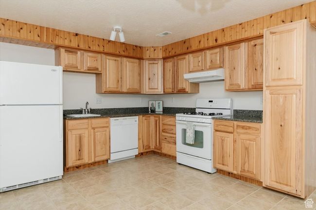 Kitchen with white appliances, under cabinet range hood, dark stone countertops, and light brown cabinetry | Image 51